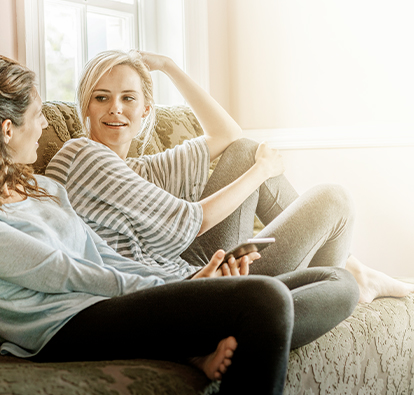 Two woman lounging on a sofa, talking.