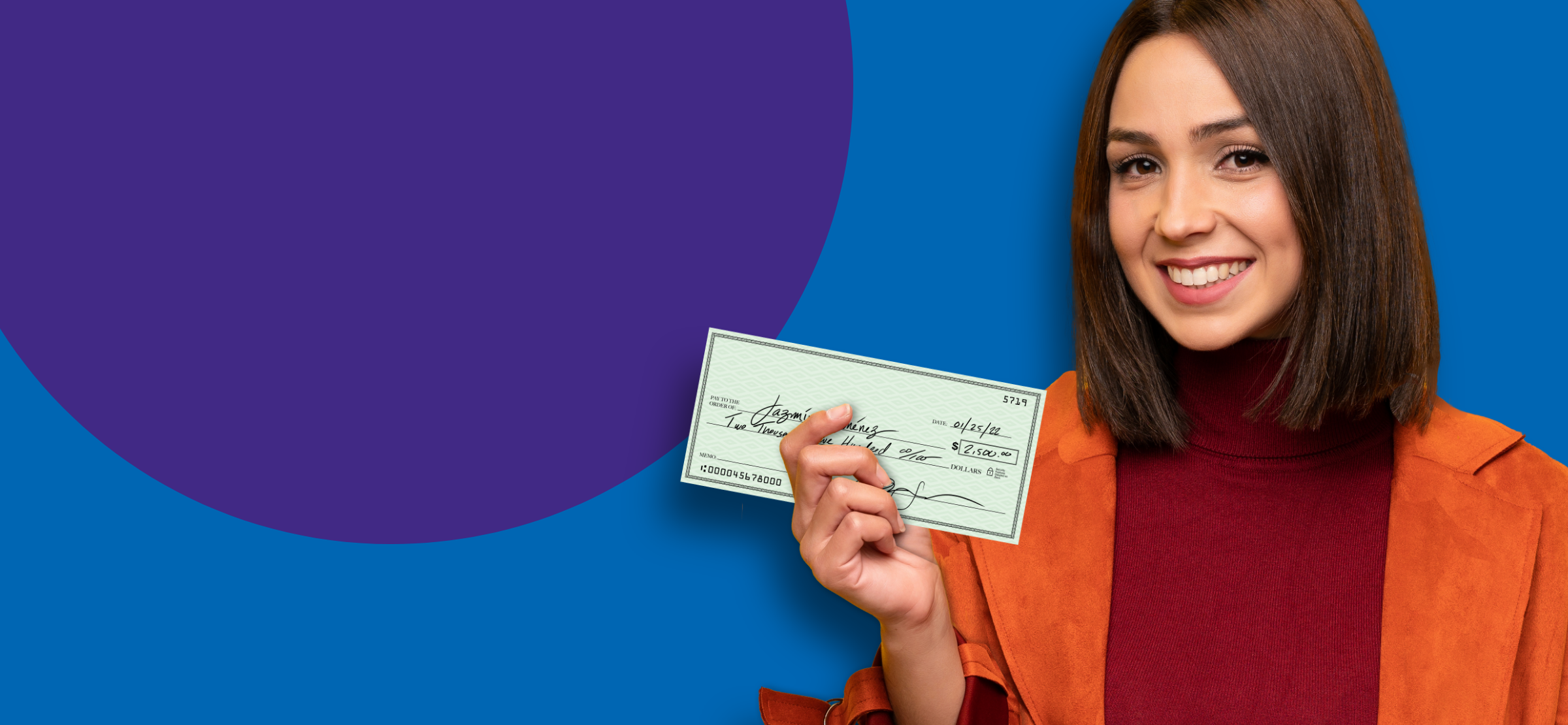 A woman in an orange coat smiling, holding a check.