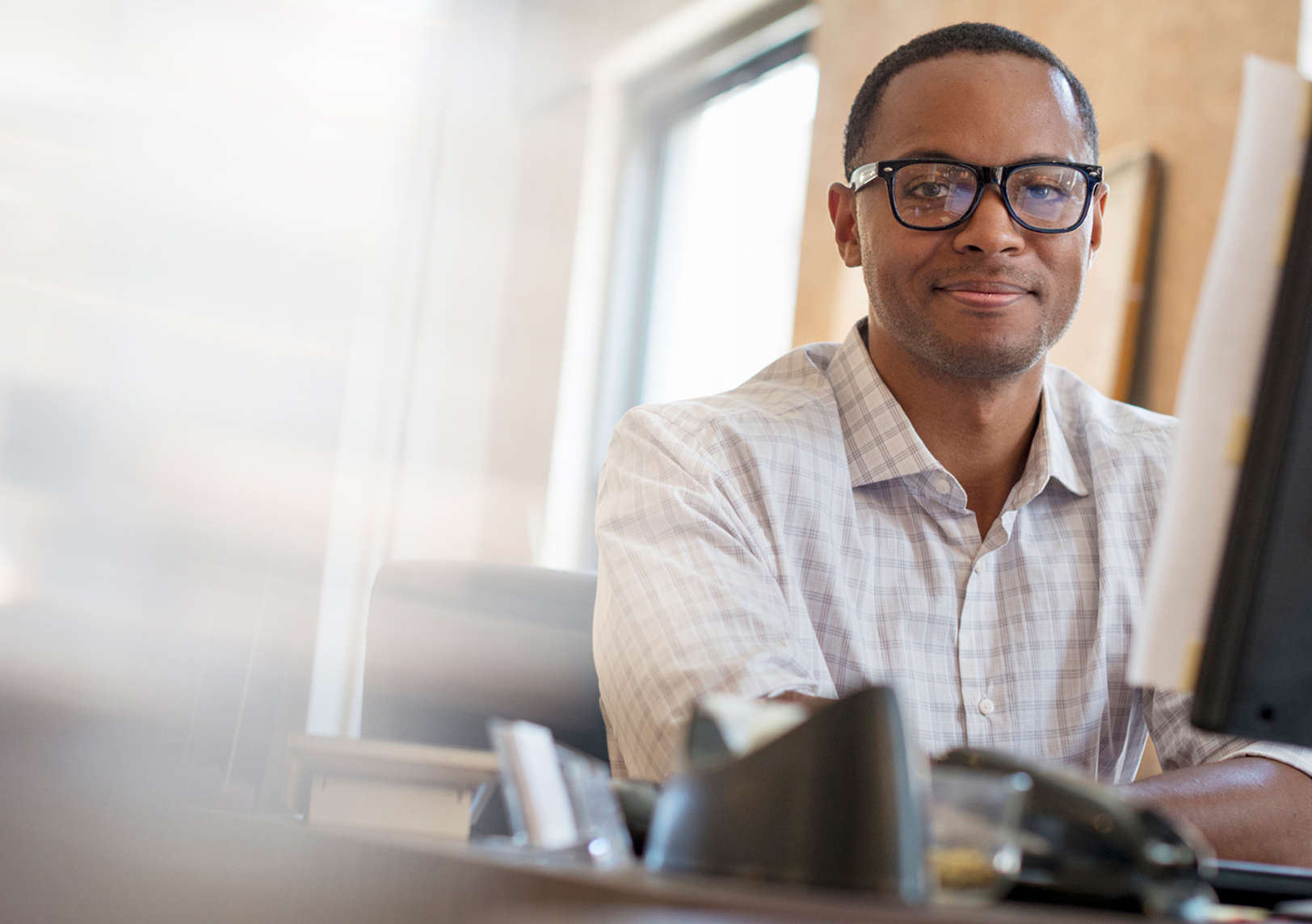 Man with glasses sitting at his desk, in front of his computer smiling.