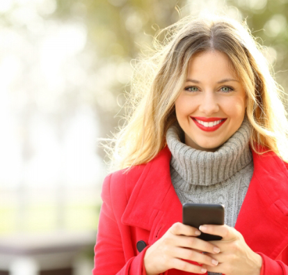 Smiling woman in red coat holding a cell phone.