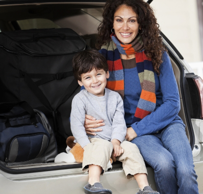 A woman and a little boy sitting in the back of an SUV with luggage behind them.