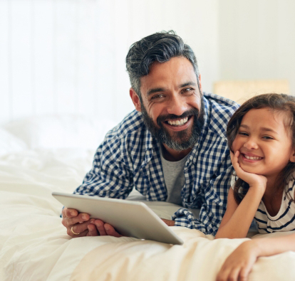 A man and a little girl smiling while looking at a tablet.