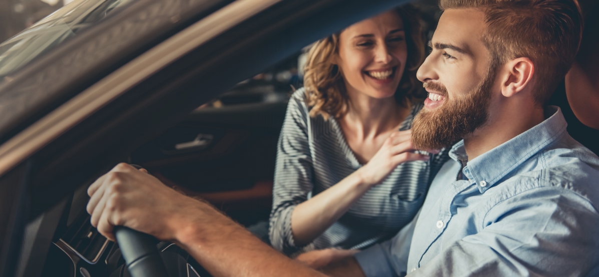 A man and a woman smiling while sitting in a car.