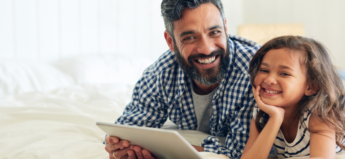 A man and a little girl smiling while looking at a tablet.