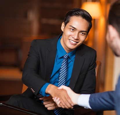 Man smiling in a suit, shaking hands with another man.