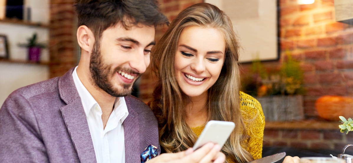 Smiling man and woman, looking on a mobile device.