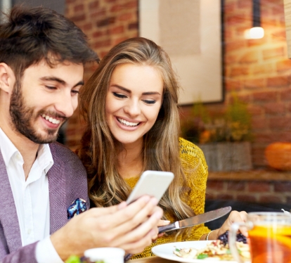 Smiling man and woman, looking on a mobile device.