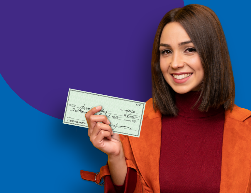 A woman in an orange coat smiling, holding a check.